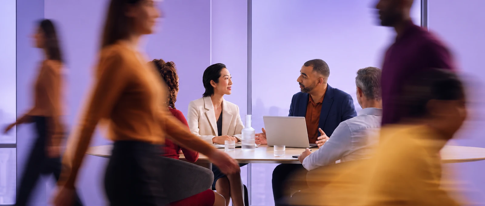 Four people around a meeting table with a laptop between them, the room moving past in blur